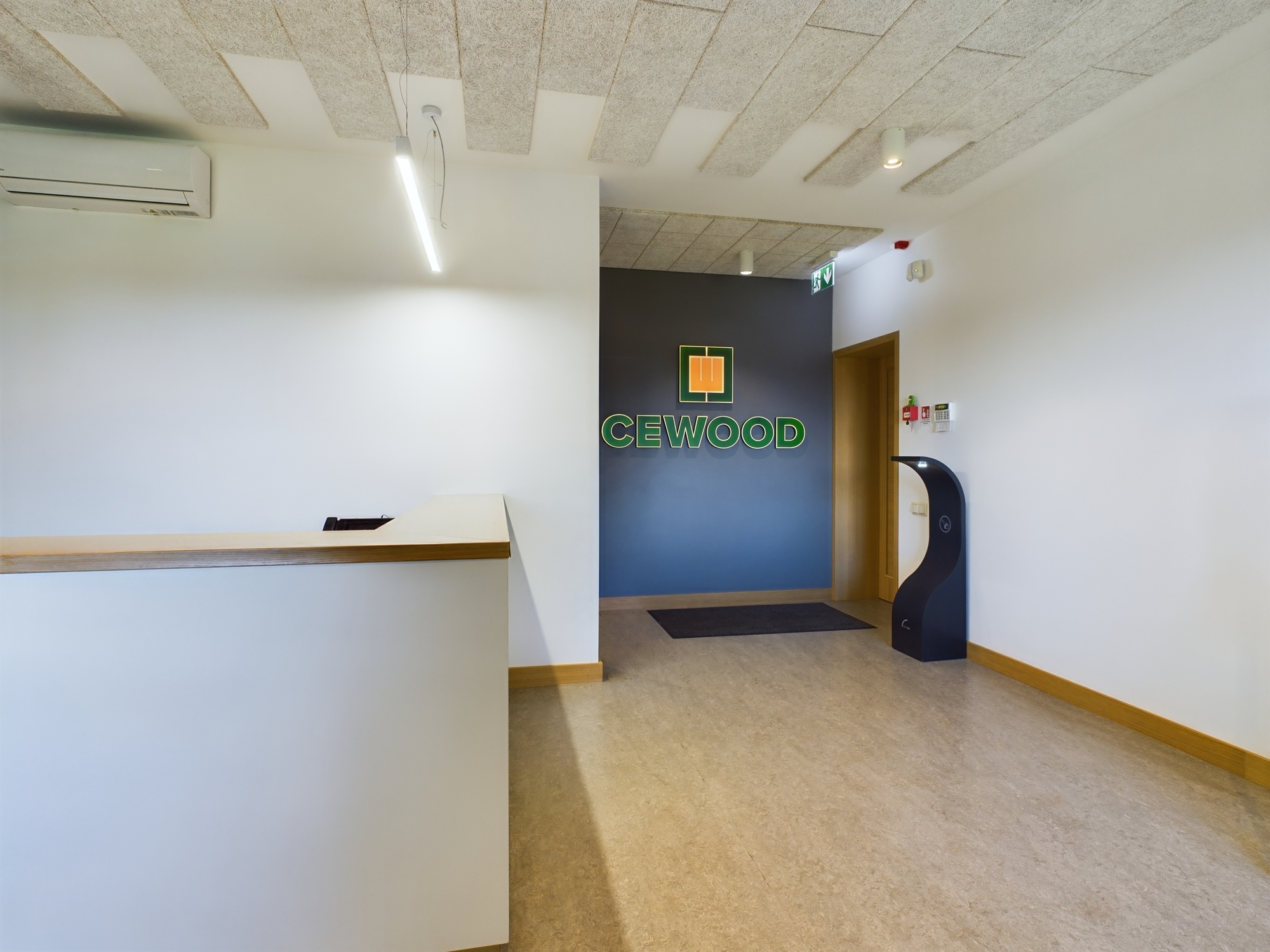 Moderna biroja recepcijas zona ar CEWOOD zīmolu uz sienas. Iebūvēts gaisa kondicionieris. Kvalitatīva komercplatību fotogrāfija.