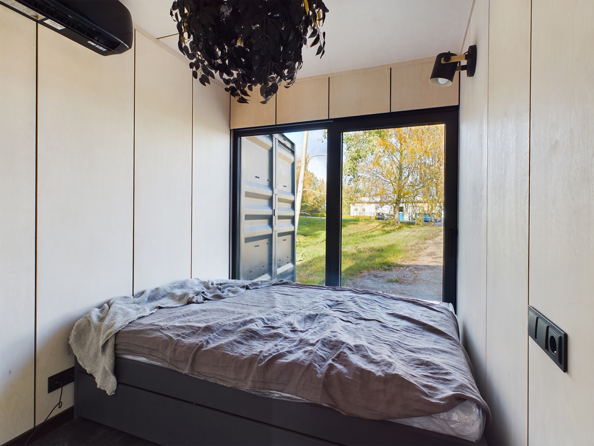 Mājīga guļamistaba ar koka sienu apdari un lielu logu. Kvalitatīva nekustamā īpašuma fotogrāfija.