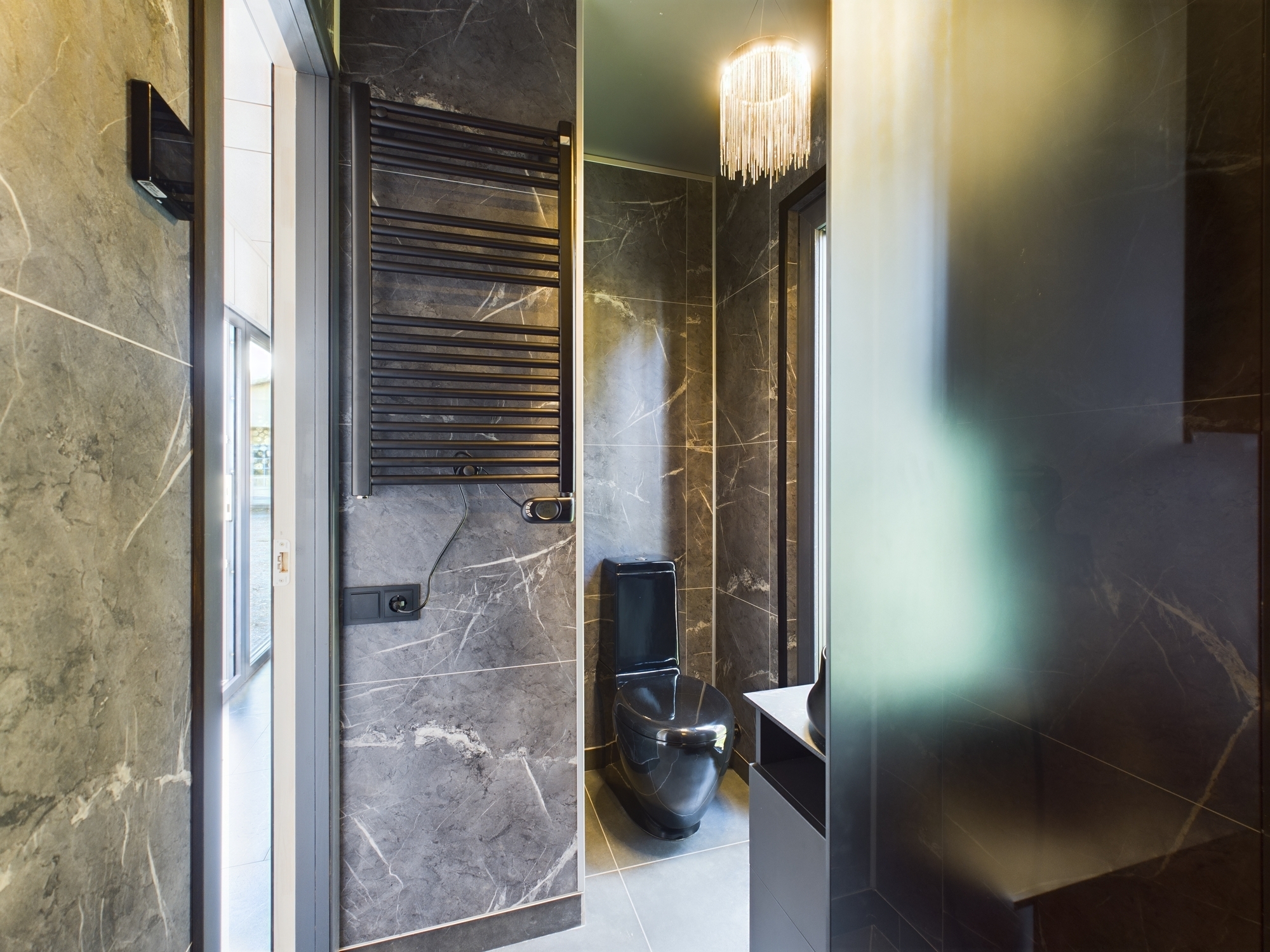 Sanmezgls ar tumšām marmora flīzēm un dvieļu žāvētāju – premium interjera fotogrāfija