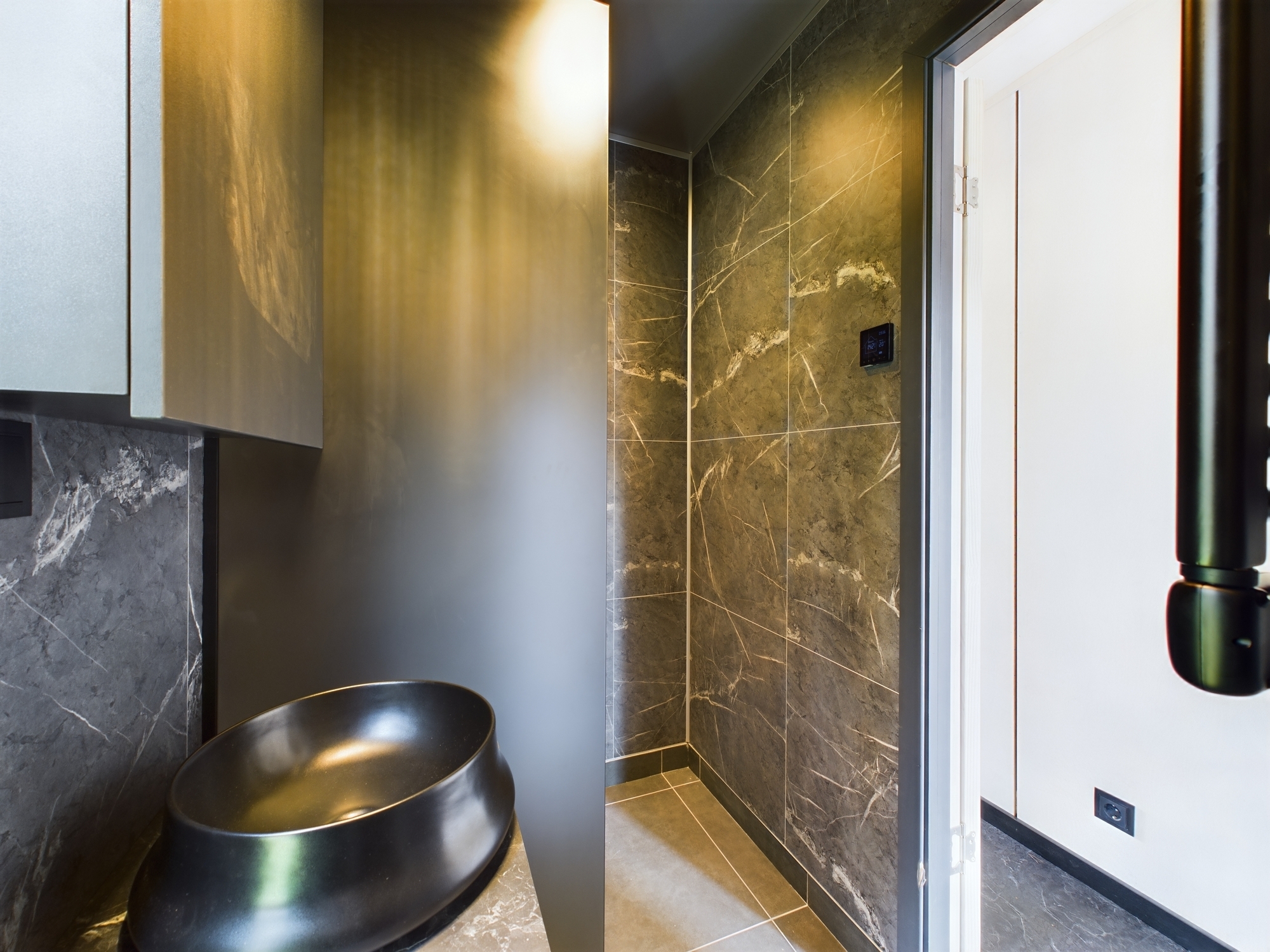 Tuvplāns: Vannas istaba ar melnu dizaina izlietni un tumšām, teksturētām flīzēm. Kvalitatīva interjera fotogrāfija.