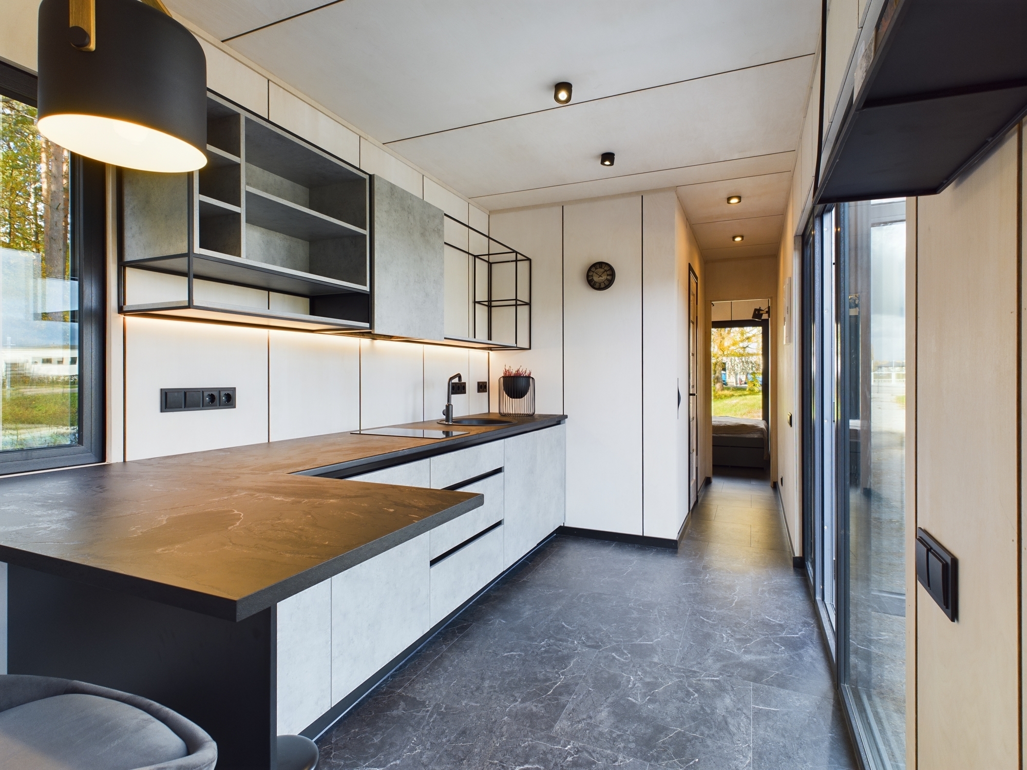 Moderna, šaura virtuve ar tumšu virsmu un atvērtiem plauktiem. Kvalitatīva nekustamā īpašuma fotogrāfija.