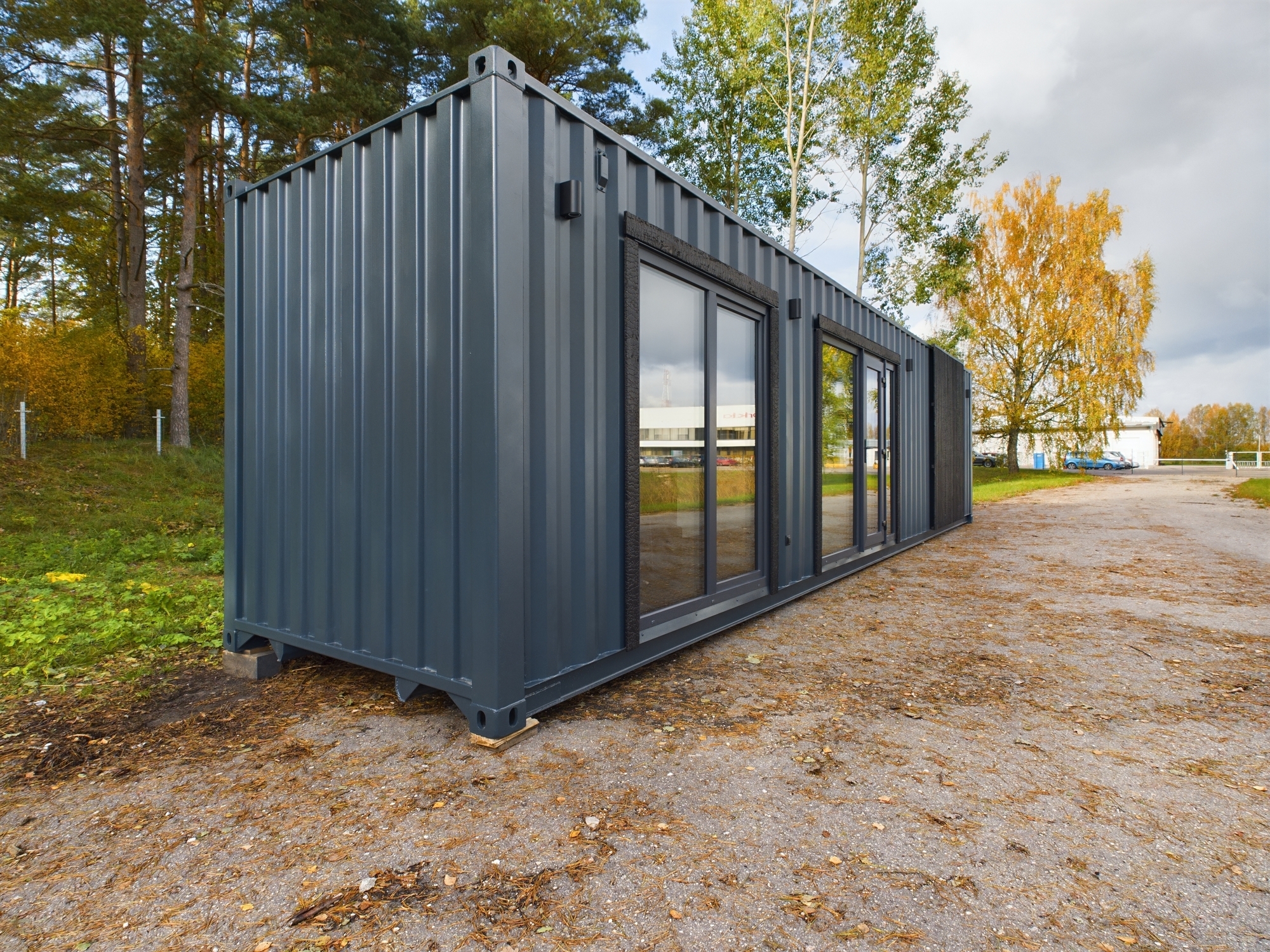 Tuvplāns: Tumši pelēka moduļu māja ar metāla apdari un garām stikla logu joslām. Kvalitatīva nekustamā īpašuma fotogrāfija.
