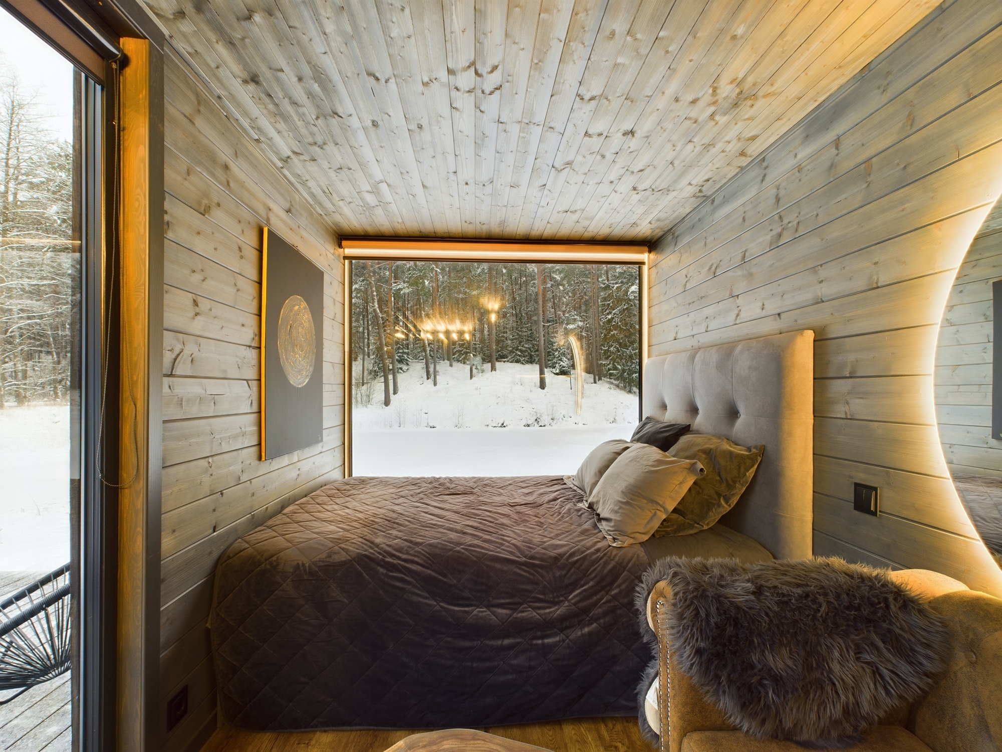 Ērta guļamistaba ar gultu un plašu panorāmas logu, kas sniedz skatu uz sniegotu mežu. Kvalitatīva nekustamā īpašuma fotogrāfija.