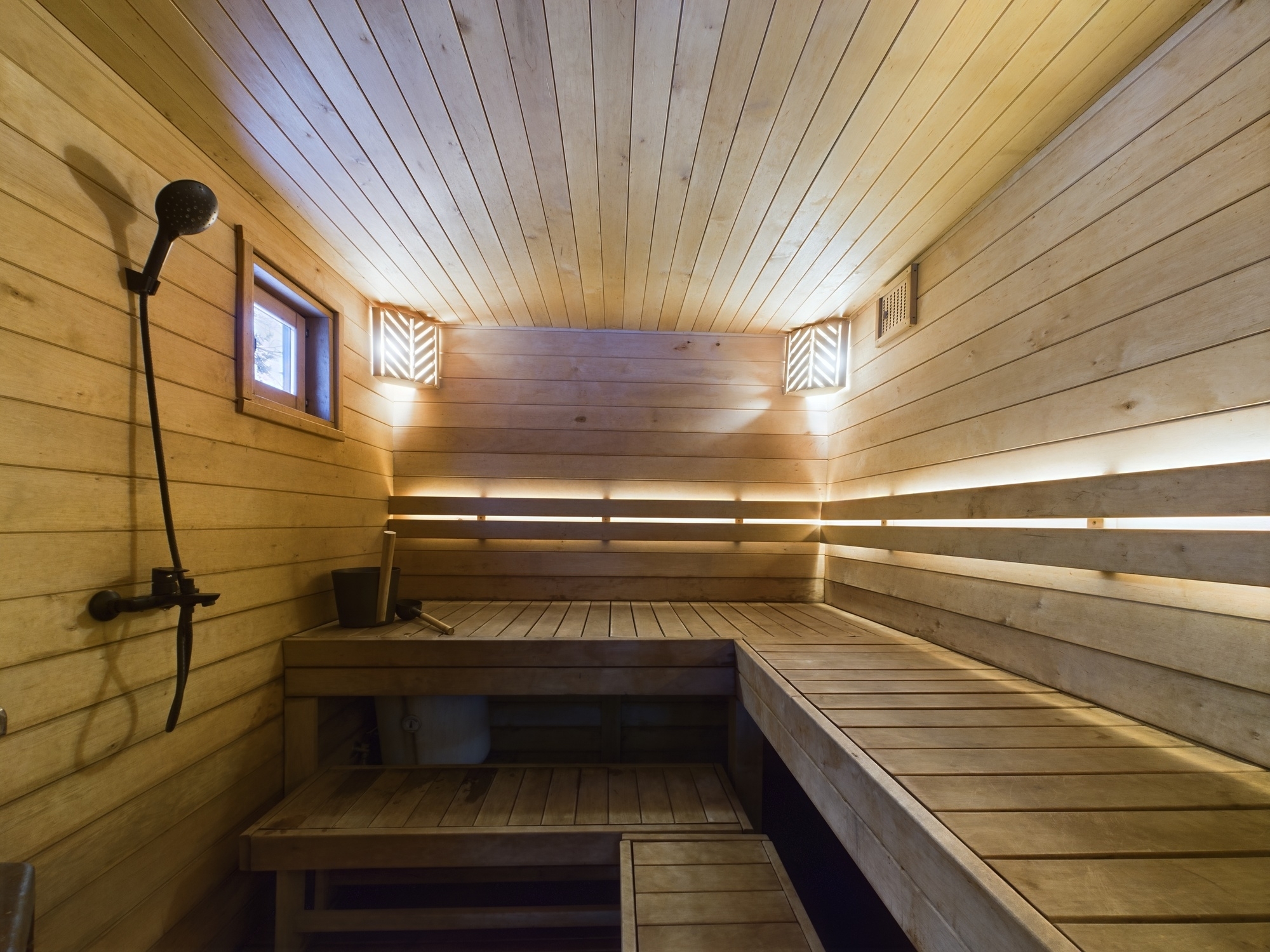 Plašs pirts interjers ar divlīmeņu koka lāvām un dušas iekārtu. Kvalitatīva nekustamā īpašuma fotogrāfija.