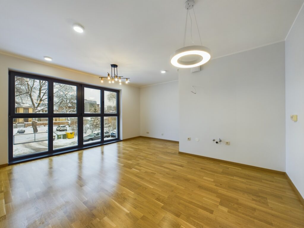 Tukša, gaiša istaba ar koka grīdu, modernu apgaismojumu un panorāmas logiem. Dzīvoklis pārdošanai Zvejnieku ielā.