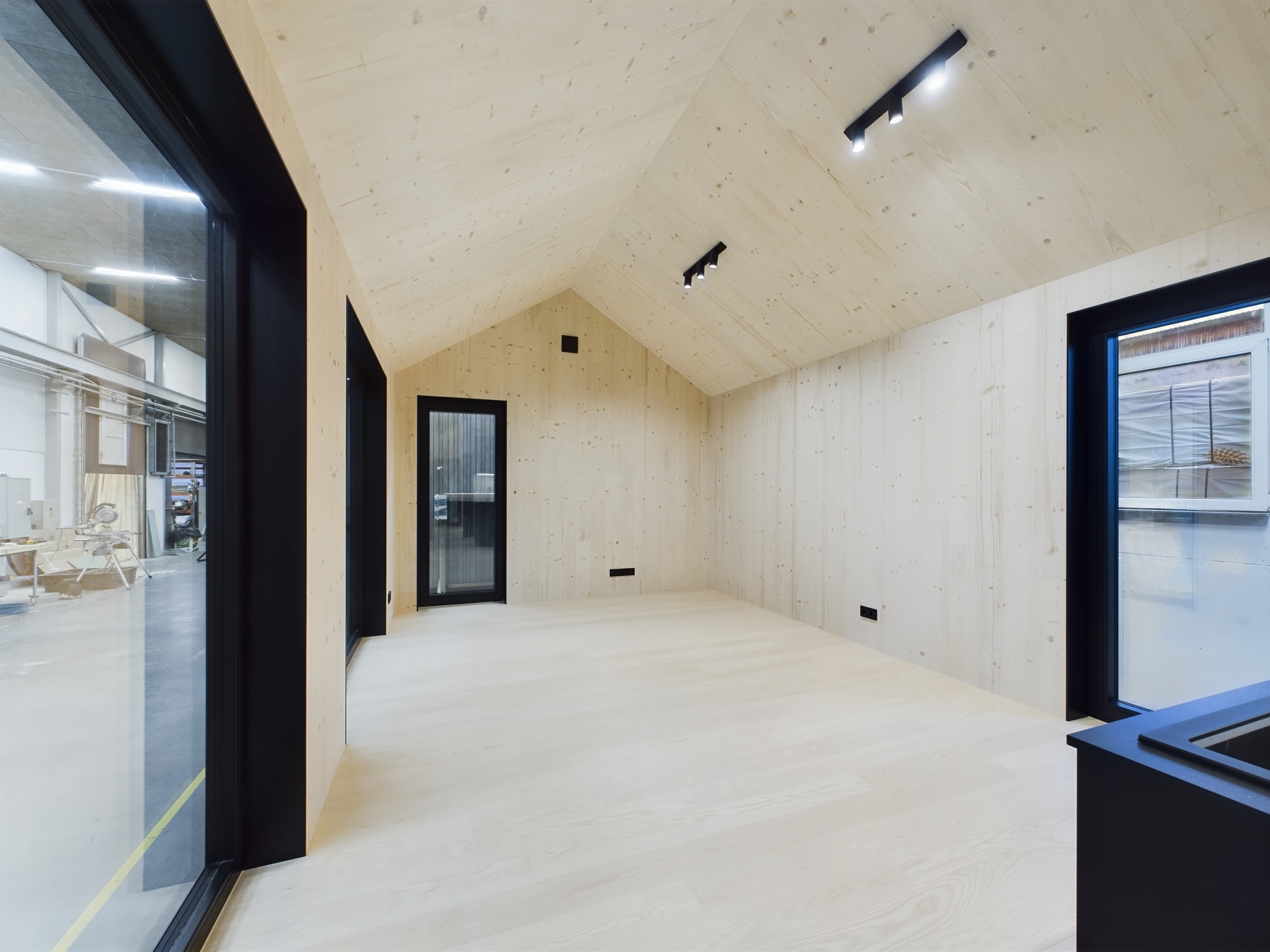 Tīra, tukša moduļu mājas telpa ar augstiem koka griestiem un lieliem logiem. Kvalitatīva arhitektūras fotogrāfija.