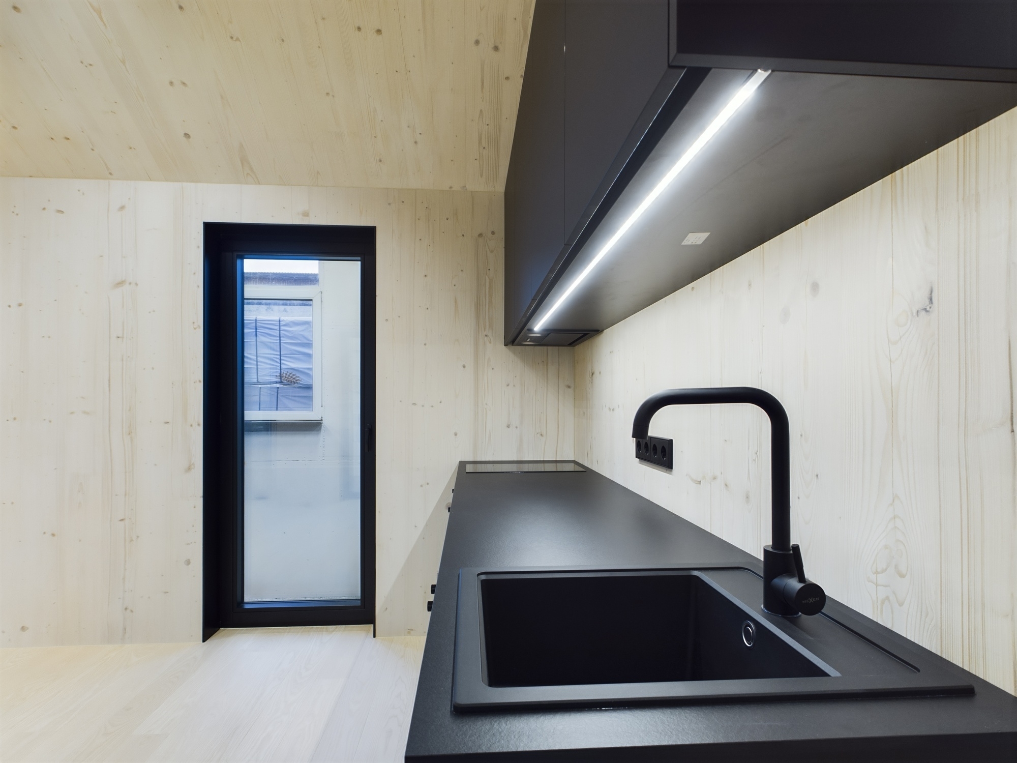 Tuvplāns: Melna izlietne, jaucējkrāns un LED apgaismojums zem virtuves skapjiem. Kvalitatīva virtuves interjera fotogrāfija.