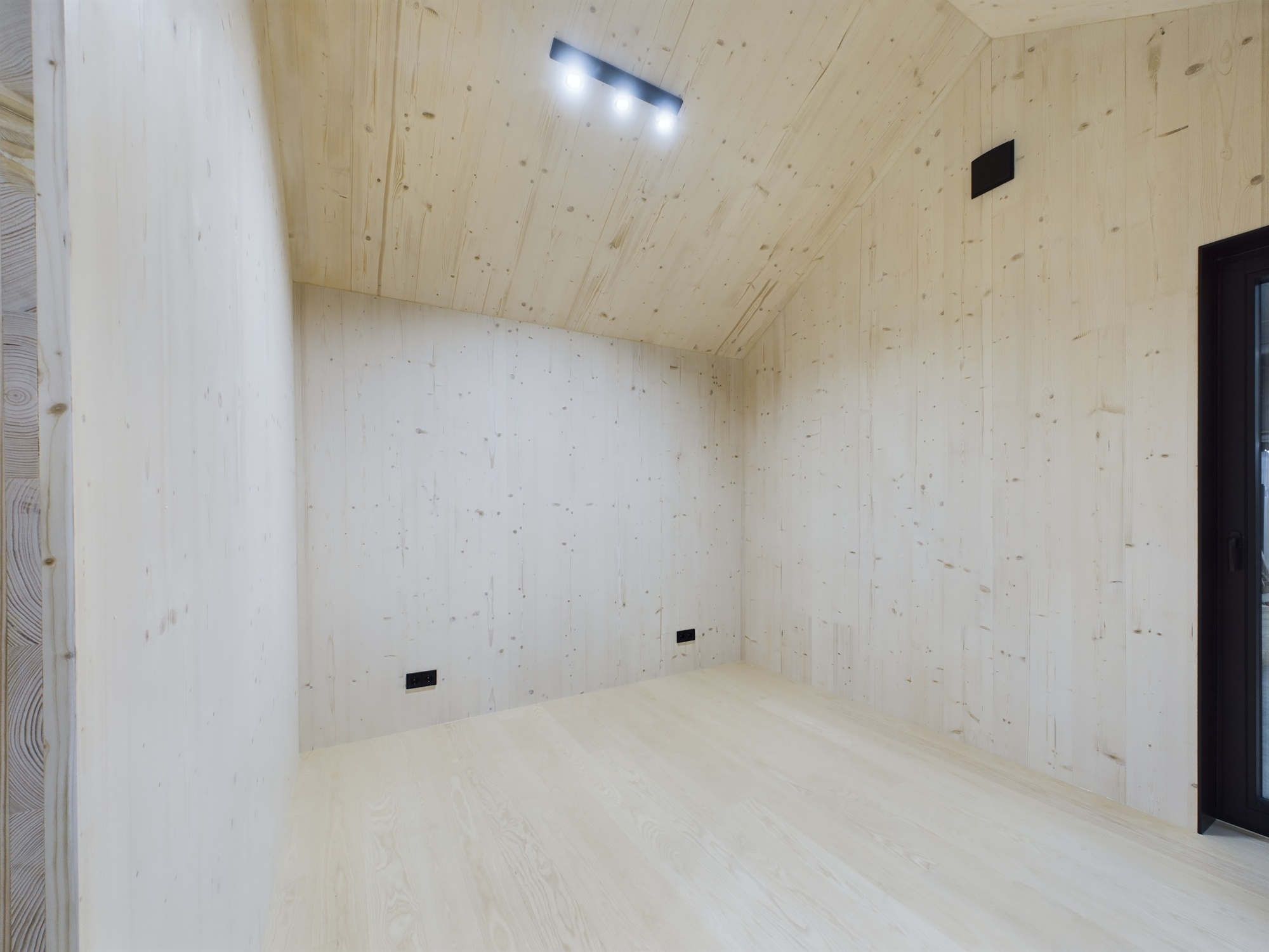 Tīra un gaiša moduļu mājas telpa ar koka sienām un griestiem. Iebūvēts griestu apgaismojums. Kvalitatīva arhitektūras fotogrāfija.