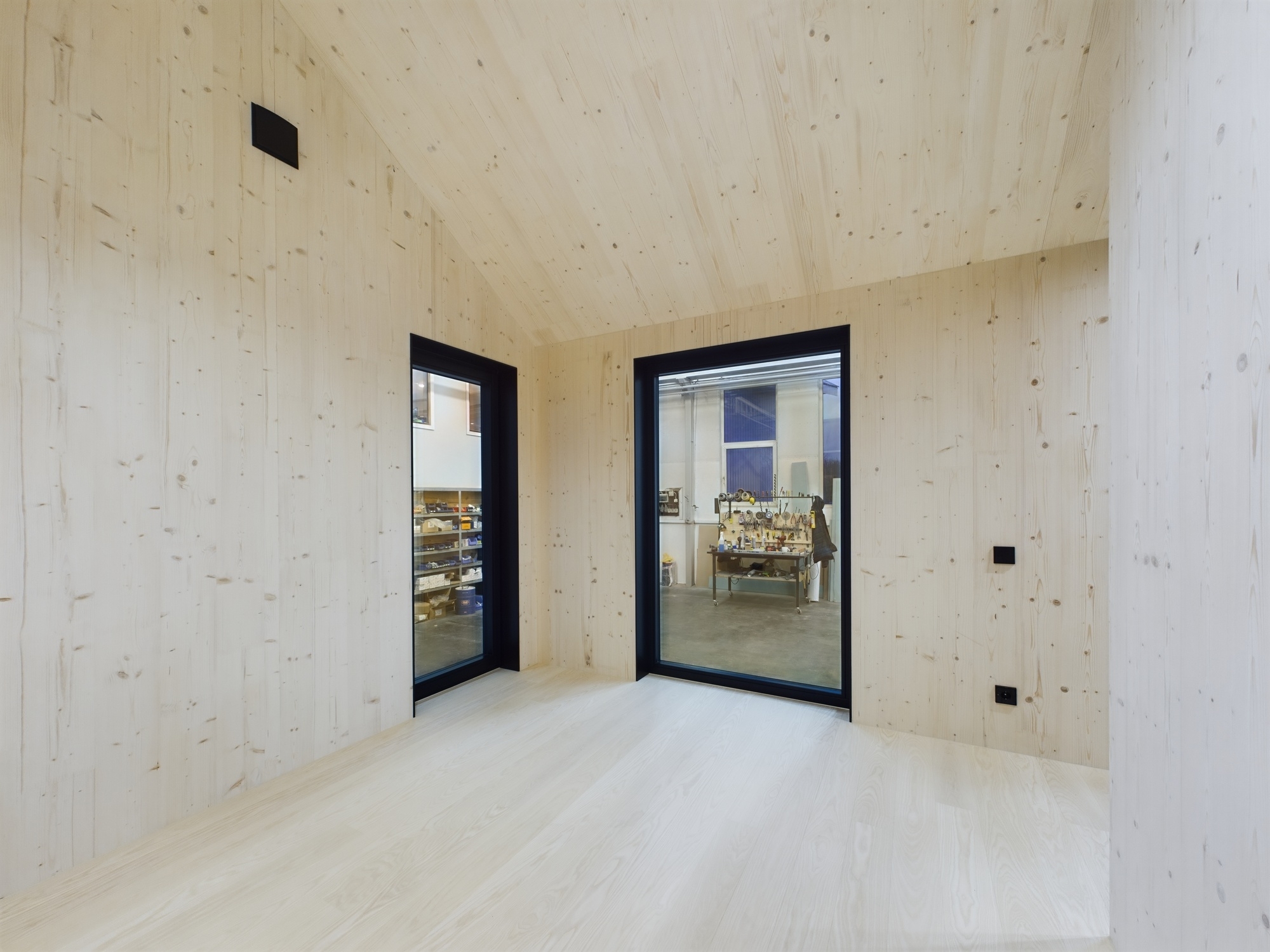 Tīra, tukša telpa ar gaišu koka apdari, kas demonstrē augstas kvalitātes melni kadrētus logus. Kvalitatīva arhitektūras fotogrāfija.