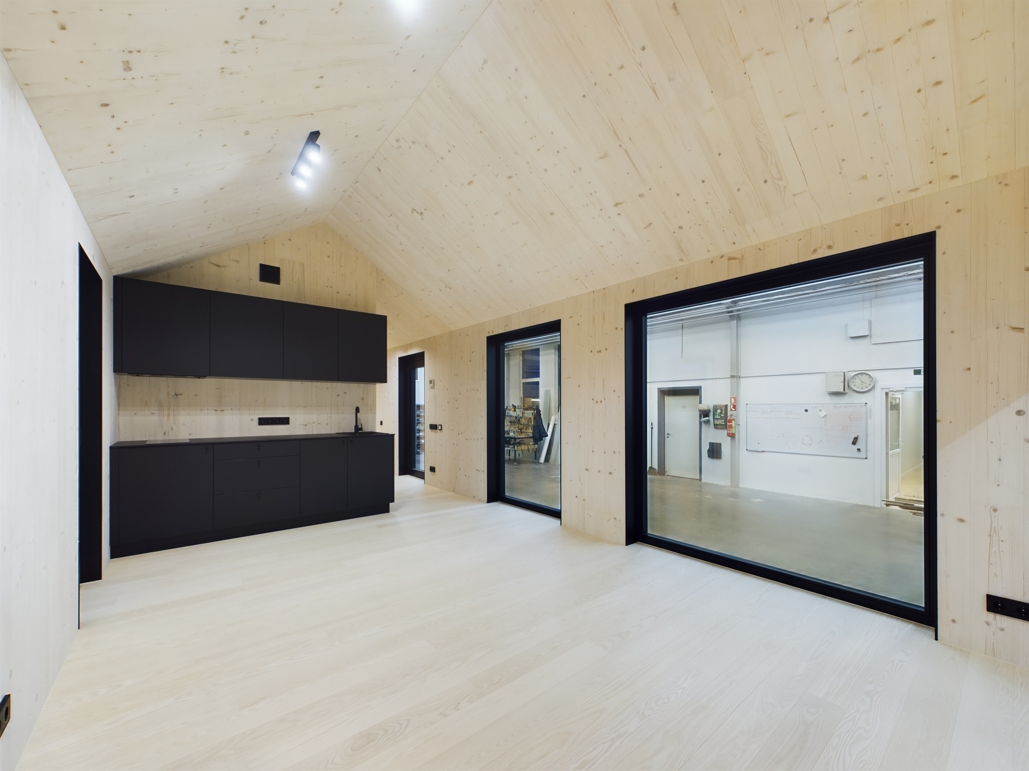 Plaša, minimālisma stila telpa ar augstiem koka griestiem un lieliem logiem. Kvalitatīva moduļu mājas interjera fotogrāfija.