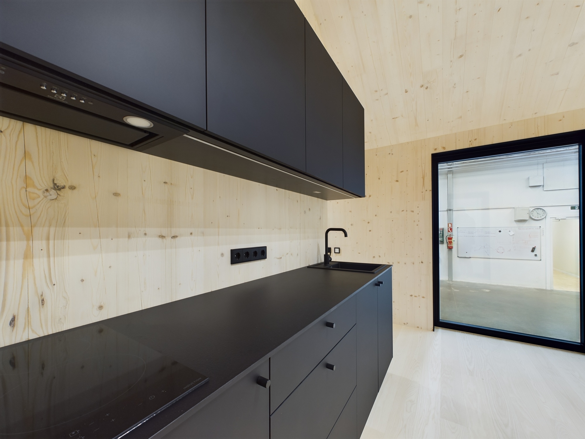 Tuvplāns: Melni, matēti virtuves skapji un virsma. Kontrasts ar gaišajām koka sienām moduļu mājā. Kvalitatīva fotogrāfija.