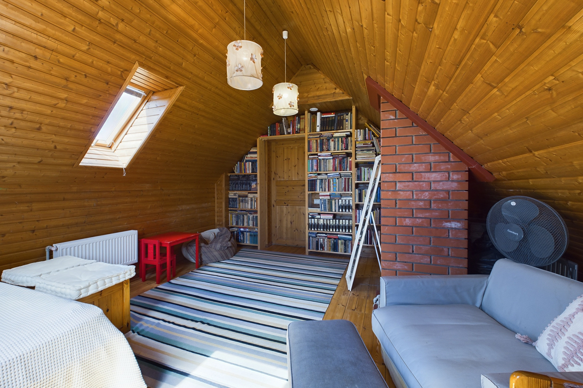Mansarda telpa ar koka apdari, jumta logu, bibliotēku un gultu. Kvalitatīva interjera fotogrāfija.