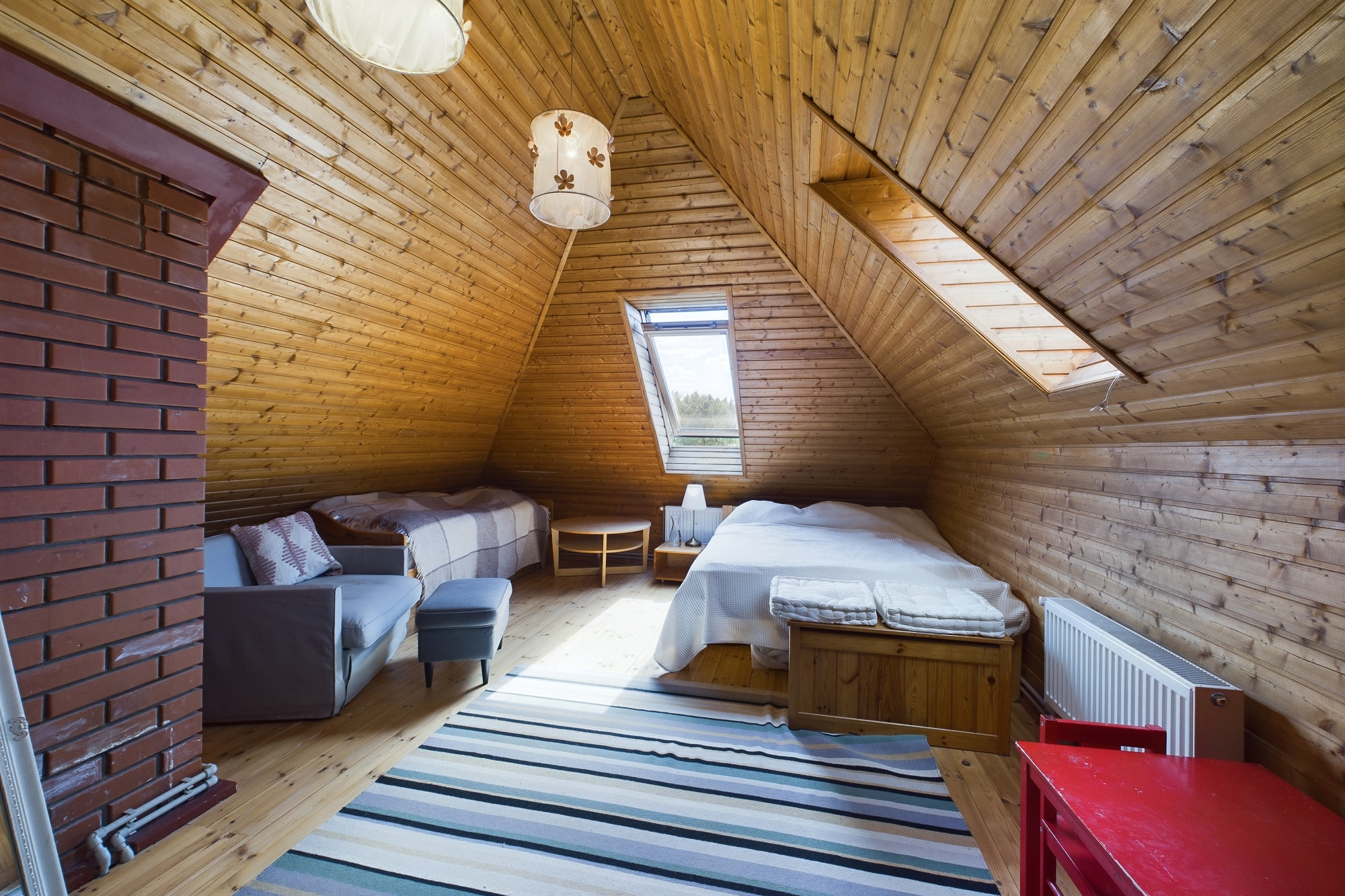 Mājīga guļamistaba bēniņos ar koka sienām, jumta logu un divām gultām. Kvalitatīva interjera fotogrāfija.