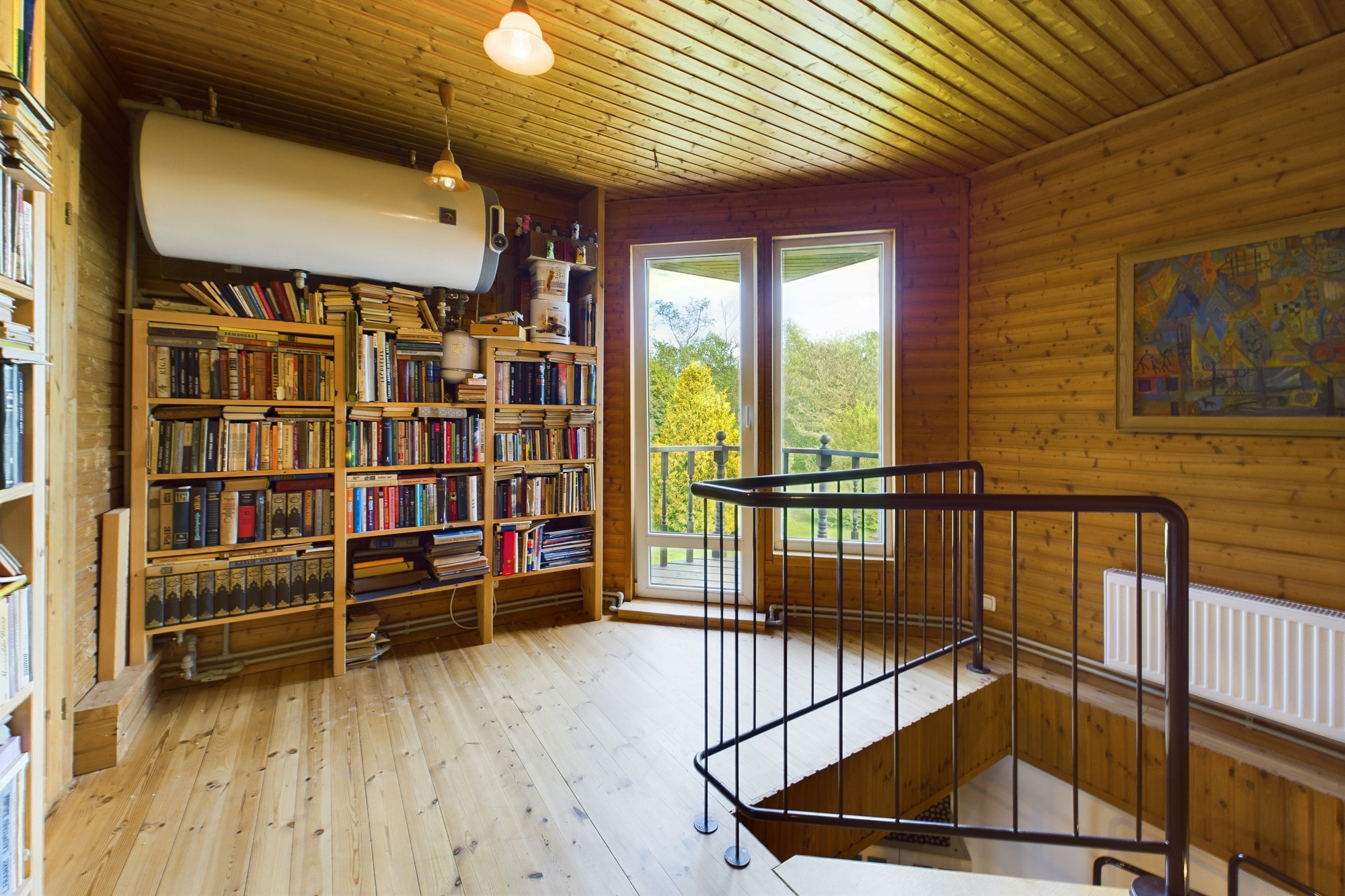 Gaiša mansarda atpūtas zona ar iebūvētu grāmatu plauktu un skatu uz āru. Kvalitatīva interjera fotogrāfija.