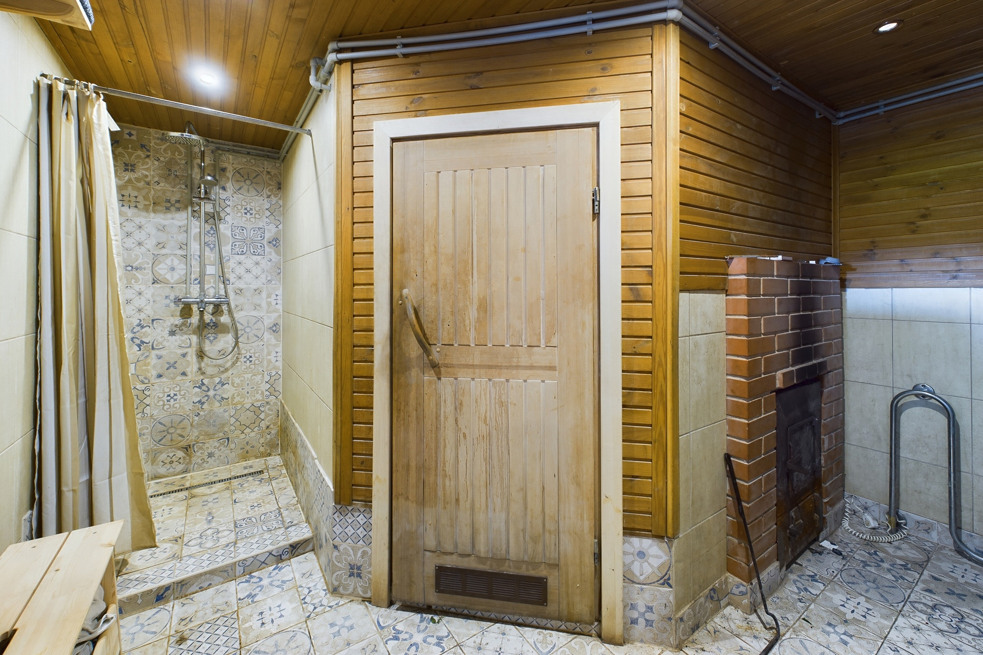 Funkcionāla dušas telpa ar pirts krāsns elementu un koka sienu apdari. Kvalitatīva interjera fotogrāfija.