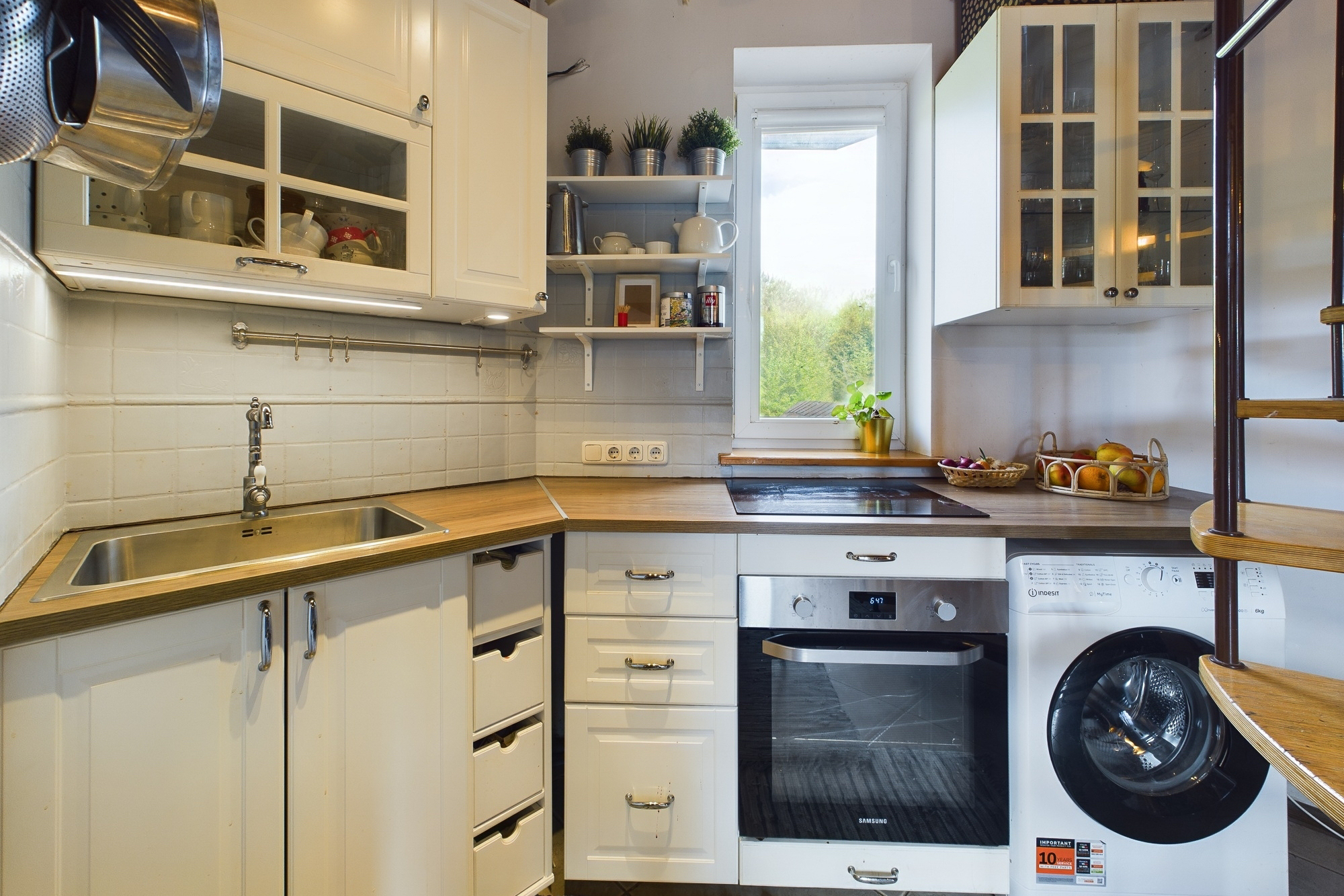Kompakta, gaiša virtuve ar koka virsmu un integrētu veļas mašīnu. Kvalitatīva interjera fotogrāfija.