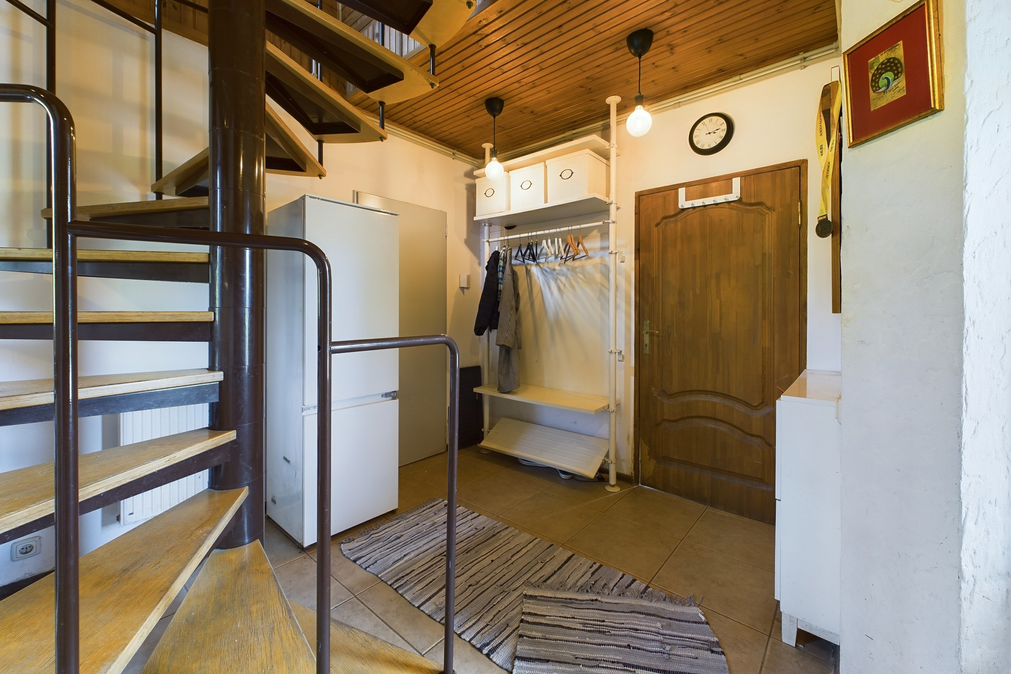 Funkcionāls priekšnams ar spirālveida kāpnēm uz augšstāvu un atvērtiem plauktiem. Kvalitatīva interjera fotogrāfija.