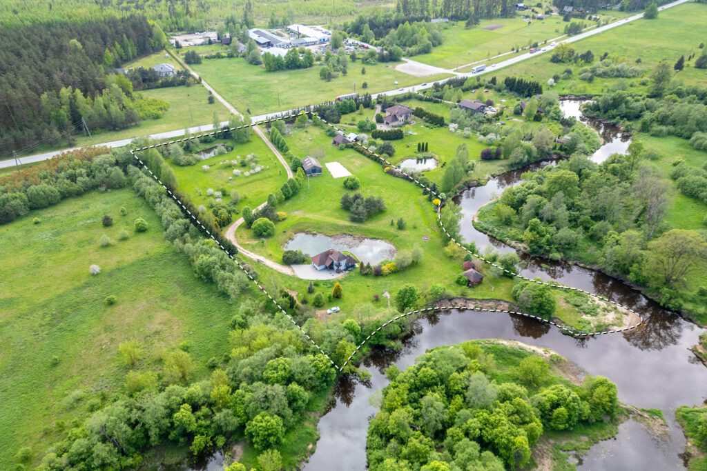 Drona skats: Investīciju zemes gabals ar atzīmētām robežām, upi un mājokļiem. Kvalitatīva nekustamā īpašuma fotogrāfija.