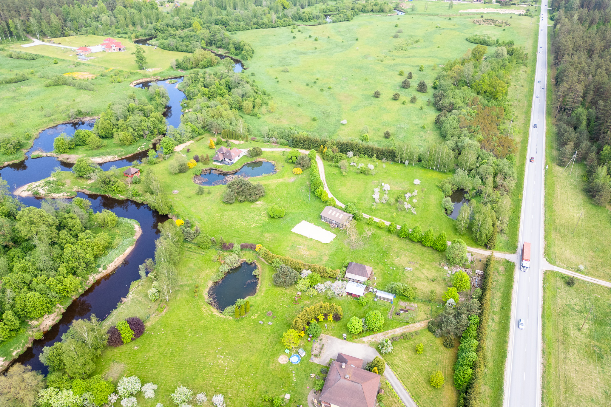 Ekskluzīvs drona kadrs parāda privātmāju apbūves potenciālu pie ceļa un ūdenstilpēm.