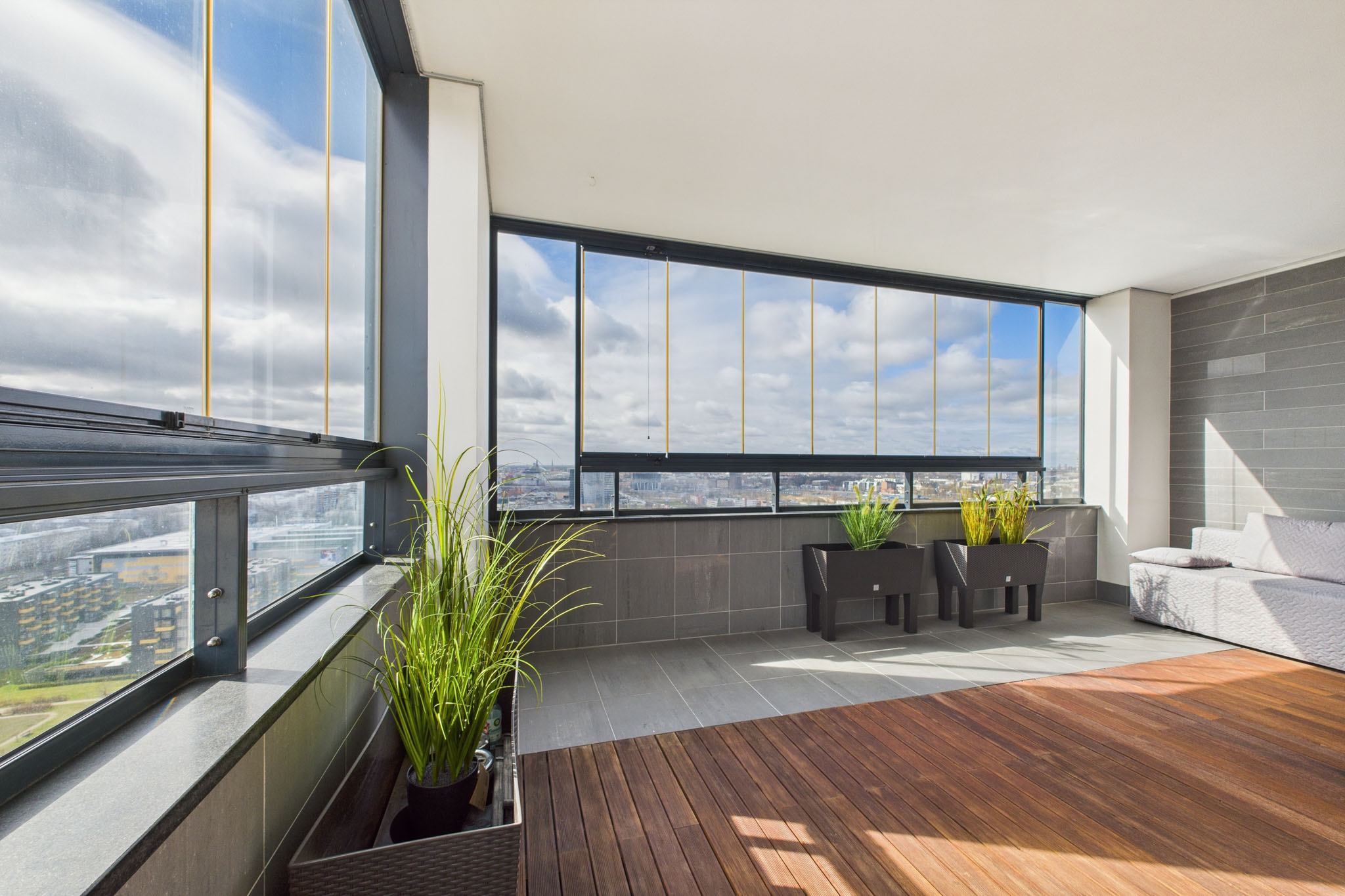 Mūsdienīga dzīvokļa interjers: Slēgta lodžija ar koka grīdu un augstceltnes skatu – nekustamā īpašuma fotogrāfijas