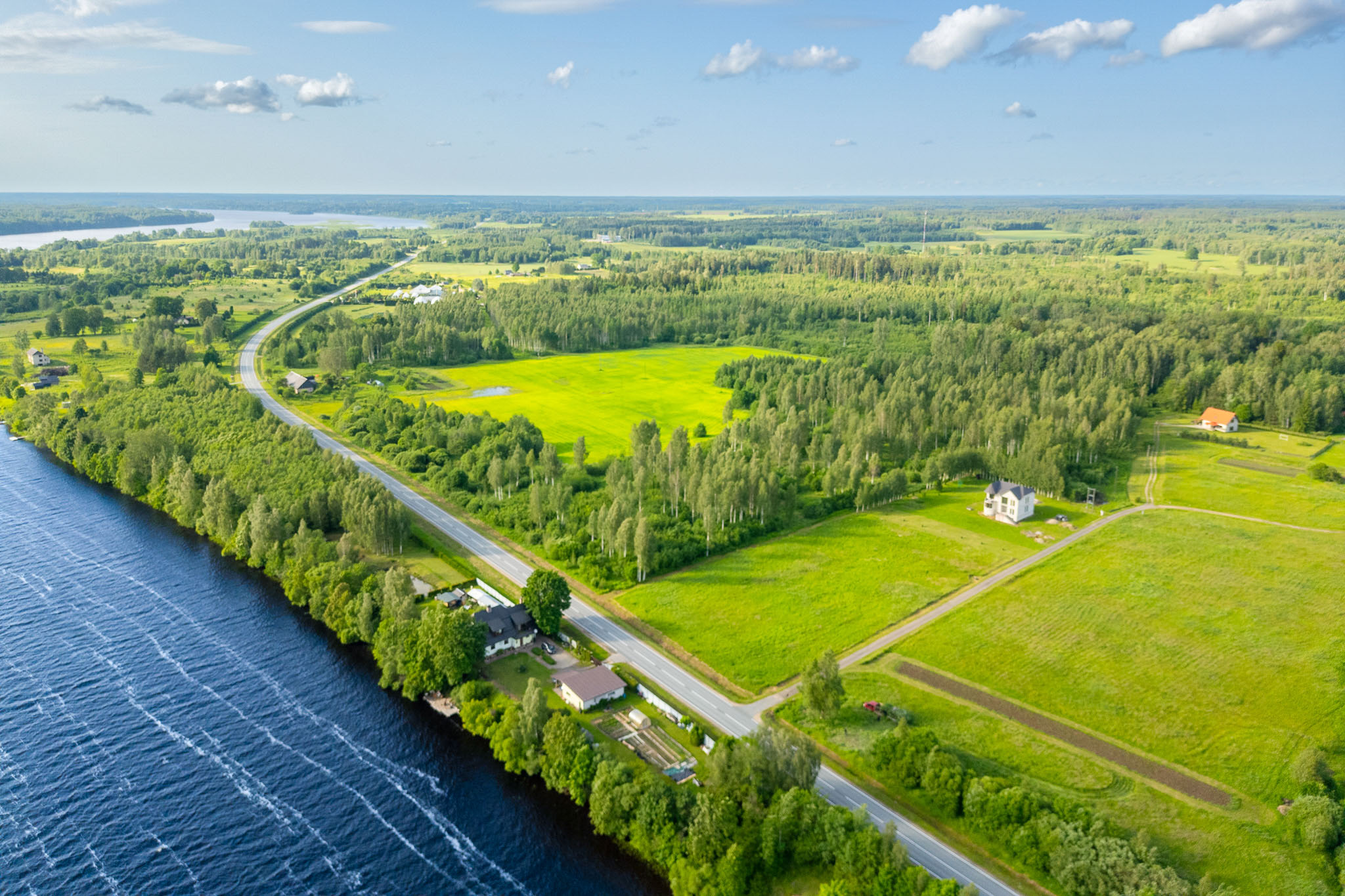 Ainavisks drona skats: Zemes gabali pie upes/ezera ar ceļu – nekustamā īpašuma fotogrāfija